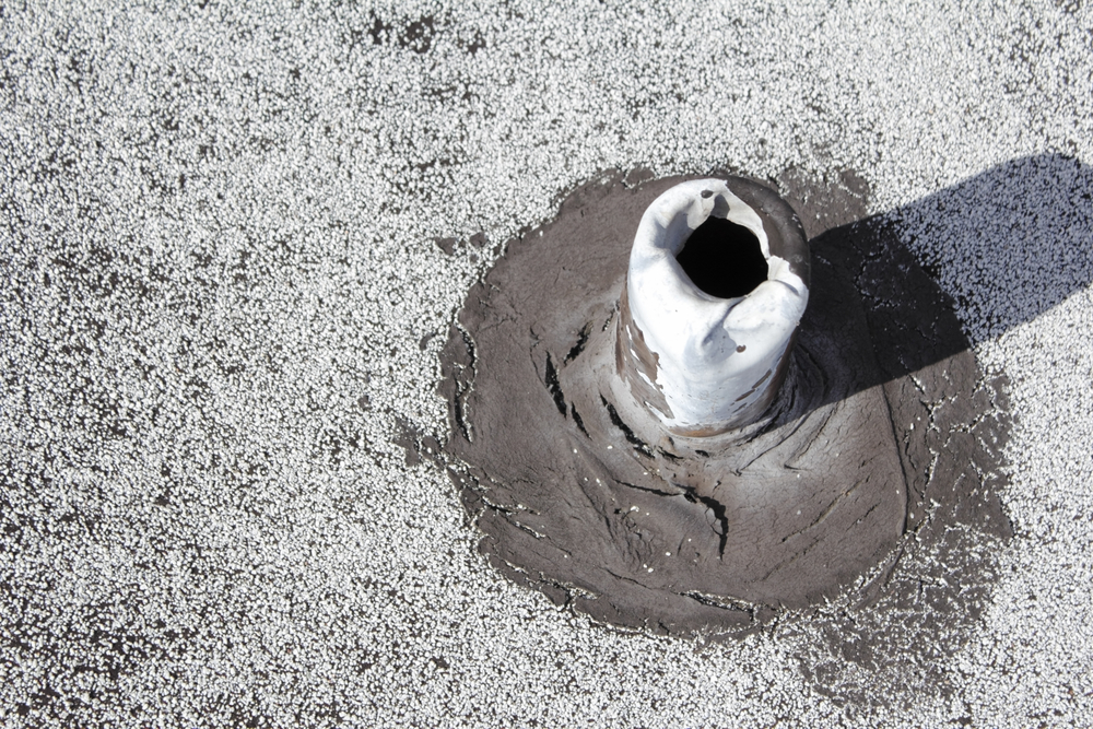 Closeup of a silver metal worn roof vent stack pipe with cracked and split black rubber boot flashing rotting and disintegrating away needing to be repaired to prevent leaks.