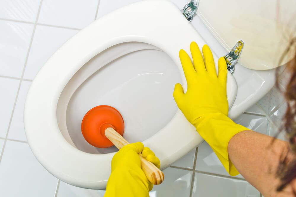 a clogged toilet is cleaned. with yellow latex gloves.