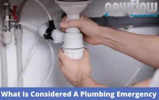 A plumber repairing a sink drain pipe, illustrating what is considered a plumbing emergency.