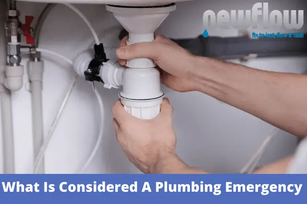 A plumber repairing a sink drain pipe, illustrating what is considered a plumbing emergency.