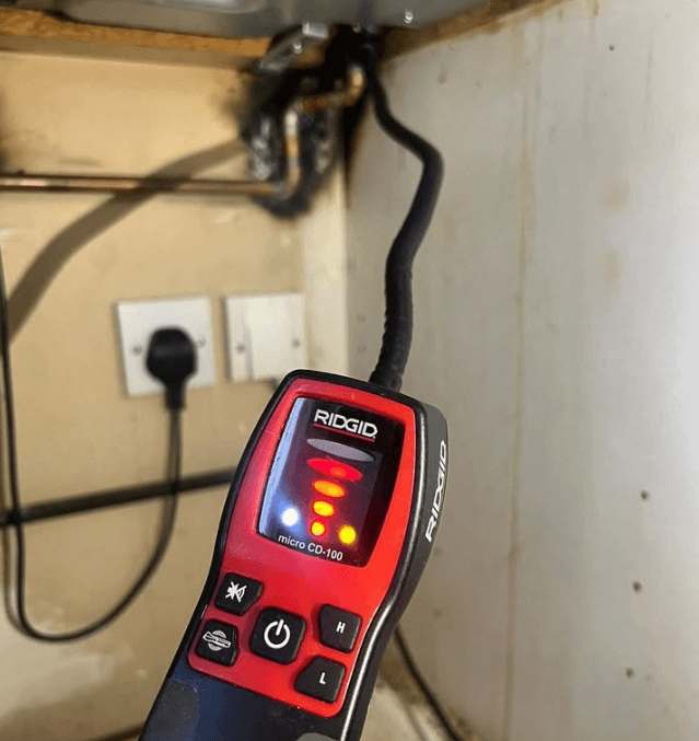 gas-leak-detector-device-inspection Handheld gas leak detector used by a plumber to identify a gas leak under a kitchen sink during inspection.