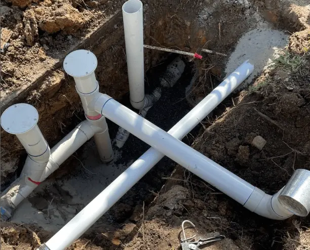 Newly installed white PVC pipes in a trench, part of a sewer system connection, surrounded by dirt and fresh concrete.
