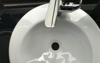 Top-down close-up of a clean white ceramic bathroom sink with a modern chrome single-lever faucet and a black pop-up drain stopper, reflecting light on its glossy surface.