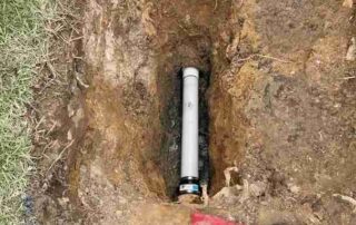 Newly installed PVC sewer pipe in an excavated trench, showing a cleanout cap and surrounding soil, indicating plumbing repair or upgrade.