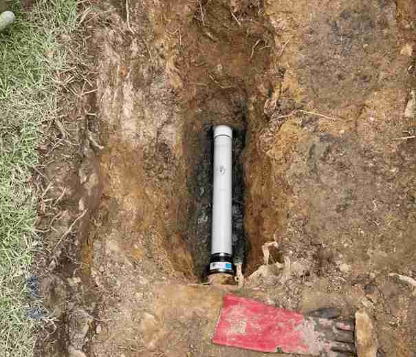 Newly installed PVC sewer pipe in an excavated trench, showing a cleanout cap and surrounding soil, indicating plumbing repair or upgrade.