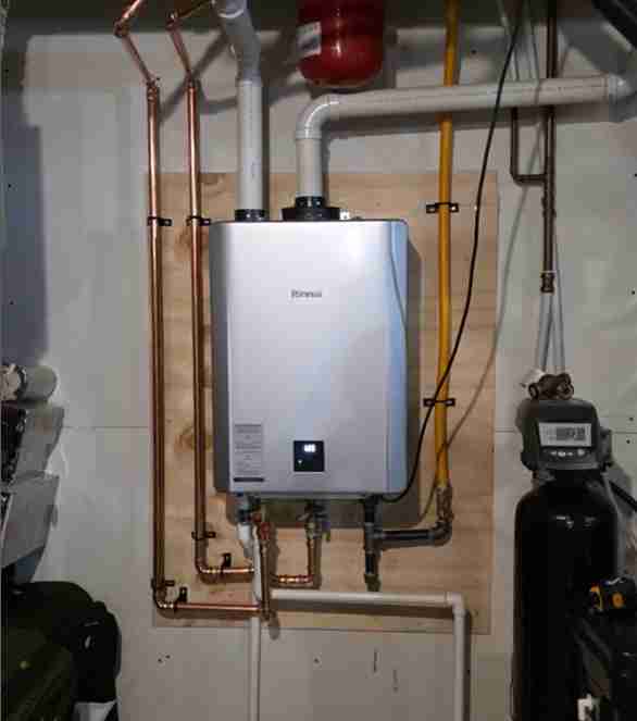 tankless-water-heater-installation A professionally installed Rinnai tankless water heater mounted on a wooden backer board, showing copper and PVC piping, adjacent to a water filtration system, typical of New Flow Plumbing's expert work