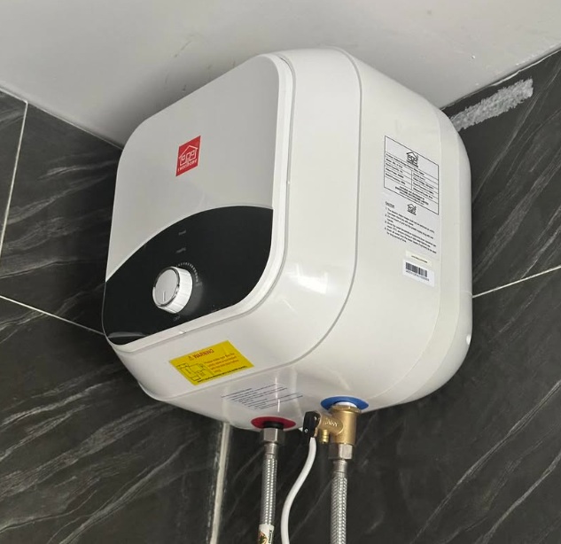 wall-mounted-electric-water-heater Wall-mounted electric water heater with temperature control knob and water inlet connections installed in a tiled bathroom corner.